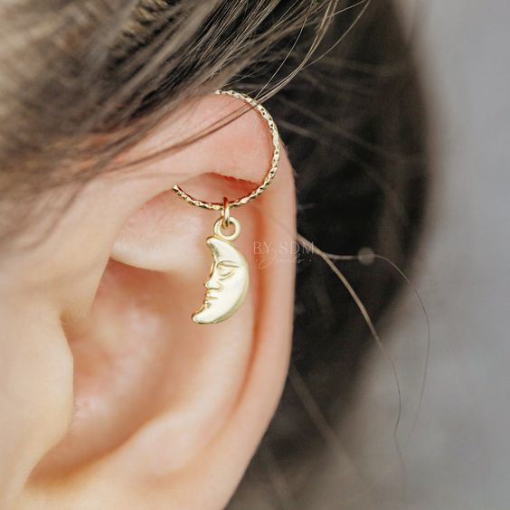 Woman with moon charm gold ear piercing. Opt for silver hoops or studs in iconic designs for a stylish Helix piercing!