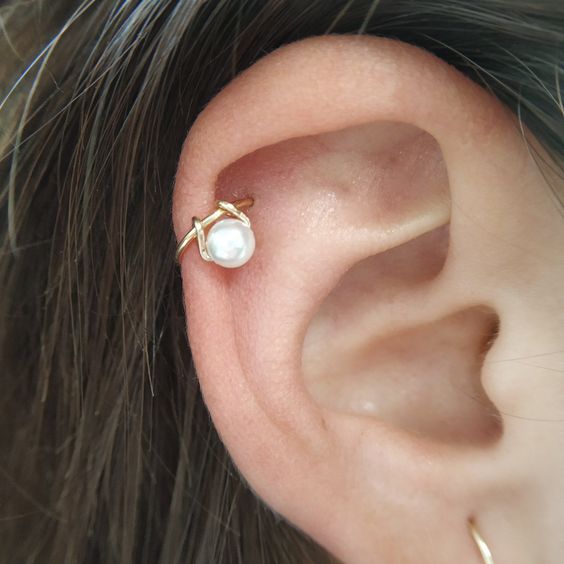 A woman's ear with a pearl and gold earring, adding a touch of bejeweled bling to her daring piercing.